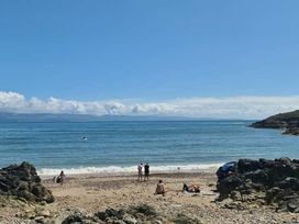 a beach scene with people by the water and rocks at Hafan y Mor Haven - Holiday Accommodation 18358 Pwllheli