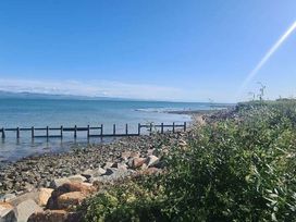 a view of a beach with water and a wooden structure at Hafan y Mor Haven - Holiday Accommodation 18358 in Pwllheli