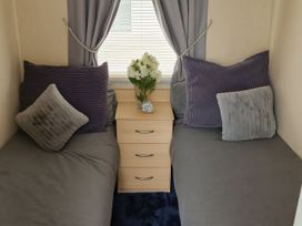 A bedroom with two beds and a side table with flowers at Millers Cottage Caravan Park - Holiday Accommodation 18845, Towyn, Abergele