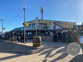 a beachfront bar with outdoor seating area and a crowd of people at Meadow Lakes Caravan Park - Holiday Accommodation 18903, Ingoldmells