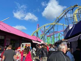a crowded amusement park street with shops and a roller coaster in the background at Seaview Caravan Park - Holiday Accommodation 18940 in Ingoldmells