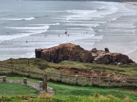 A view of surfers in the ocean near a rocky outcrop at Liskey Hill Caravan Park - Holiday Accommodation 20197, Perranporth