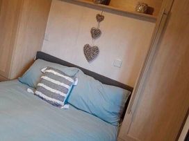 a bedroom featuring a bed with blue bedding and a cushion against a wooden wall at Hafan y Mor Haven - Holiday Accommodation 20258, Pwllheli