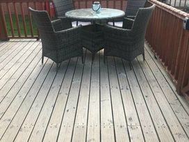 a deck area with a round table and four wicker chairs at Hafan y Mor Haven - Holiday Accommodation 20258 in Pwllheli