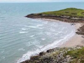 a shoreline with waves and grass-covered hills at Hafan y Mor Haven - Holiday Accommodation 20258 in Pwllheli