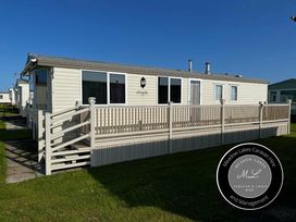 a caravan with a wooden deck and railings at Meadow Lakes Caravan Hire and Management in an outdoor setting