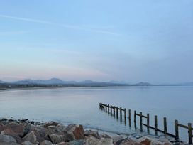 A tranquil view of the sea with a pier and mountains at Hafan y Mor Haven - Holiday Accommodation 22224 Pwllheli