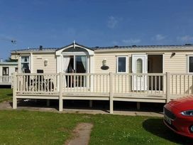 a mobile home with a deck and a red car in front at Coral Beach - Holiday Accommodation 22375 in Ingoldmells