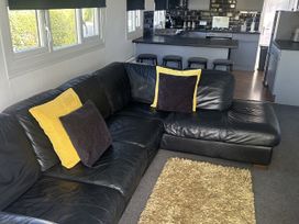 A living room with a black sofa and kitchen area at Haggerston Castle - Holiday Accommodation 3441 Berwick-upon-Tweed