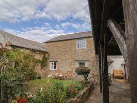 A garden with stone wall and wooden furniture at Vine Cottage in Burton Bradstock