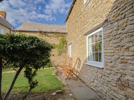 An outdoor view of a stone house with a bench and garden at Vine Cottage in Burton Bradstock