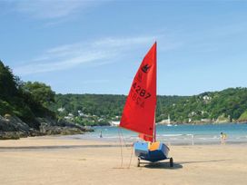 A sailboat on the beach with people walking at St Leonards in Salcombe