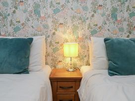 A bedroom with two beds, a lamp on a nightstand and patterned wallpaper at Farriers Yard in Whitby