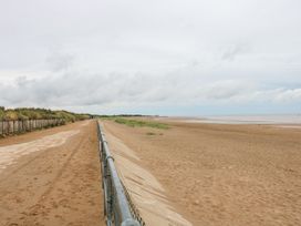 A beach with a sandy pathway and a fence at No.49 Cherry Park, Chapel St Leonards