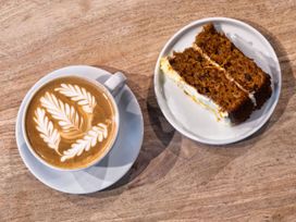 A coffee cup with latte art and a slice of cake on a plate