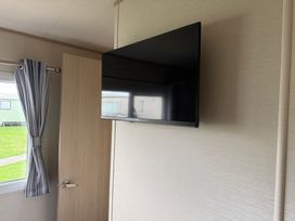 A television mounted on the wall with a curtain and a door at Ty Cariad in 
