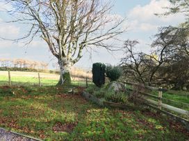 A garden with a tree, fence, and rock at 1 Fron Uchaf Parc near Bala