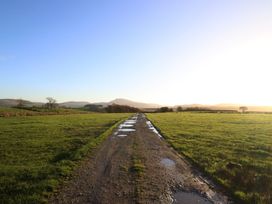 A dirt road with puddles leading through grass fields at 1 Fron Uchaf, Parc near Bala