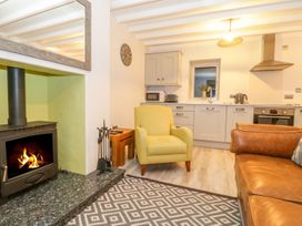 A living room with a fireplace, armchair, and kitchen area at Riverside Cottage in Conwy
