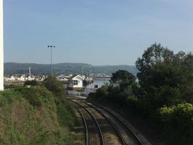 A view of train tracks leading to water and buildings at Heulfan - 17 Deganwy Castle Apartments in Deganwy