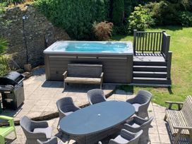 An outdoor area with a hot tub, dining table, and grill at The Old Farm House near Pelynt
