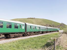 A green train moving along railway tracks near a hill at 91 Swanage Coastal Park in Swanage