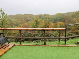 A terrace with a green surface and wooden railing overlooking a forest at Cwtch Bach Aberdare