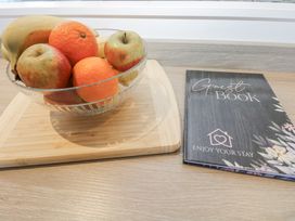 A fruit bowl with apples and oranges beside a guest book at Cosy Retreat in Pool