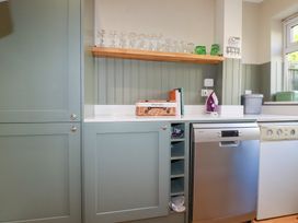 A kitchen with cabinets, glasses on a shelf, and a dishwasher at The Mizzen St Endellion near Port Isaac
