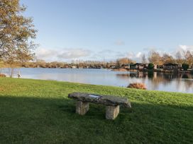 A lake with a stone bench and trees at Bluebell Lodge in Warton