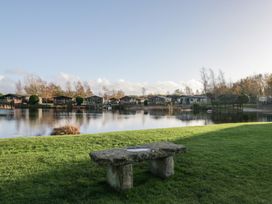 A view of cabins by a lake with a stone bench at Bluebell Lodge in Warton