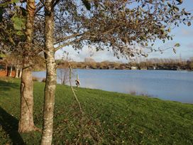 An outdoor view of a lake with trees and wooden cabins at Bluebell Lodge Warton
