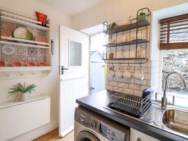 A kitchen with a sink and plates on a shelf at Periwinkle Cottage in Conwy