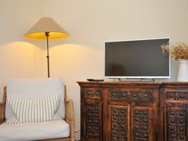 A living room with a chair, lamp, television, and cabinet at Copper Mine Cottage, Trelill near Port Isaac