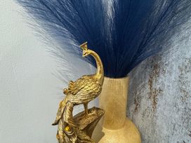 A decorative vase with a peacock sculpture and blue plant fibers
