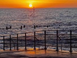 A sunset over the ocean with a railing and posts at a pier