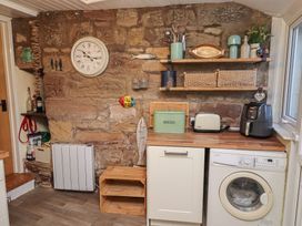 A kitchen with a washing machine and wooden shelves at Corner Cottage in Seahouses