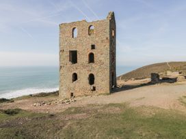 A ruined stone building with windows overlooking the ocean at Blowing House Cottage, Perranporth