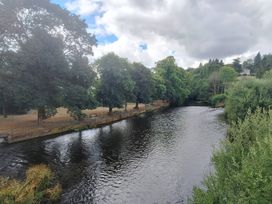 A river with trees and benches along the banks at Capel Llani Llanidloes