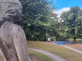A statue overlooking a river with trees and a pathway at Capel Llani in Llanidloes