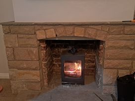 A fireplace with a wood stove and stone mantel at Fisherman's Cottage