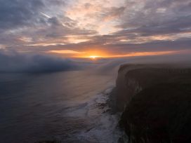 A sunset over the ocean with fog and cliffs at Fisherman's Cottage