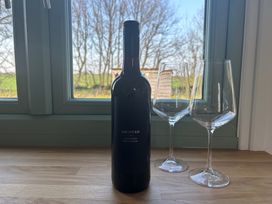 A wine bottle and two glasses by a window at Y Nyth