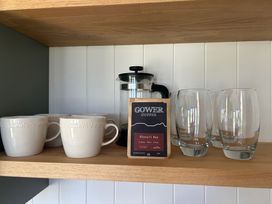 A kitchen shelf with cups, coffee grinder, coffee bag, and drinking glasses at Y Nyth in 
