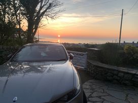 A car parked with a view of the sunset over the ocean at Bwthyn Nain