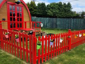 A wooden structure with a red fence and flower pots in the garden at St Austell Glamping