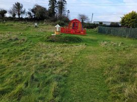 A red cabin with a fence and path in a grassy area at St Austell Glamping