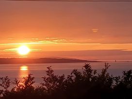 A sunset over the ocean with clouds and an island in the distance at Blue Haven Penmaenmawr