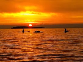 A sunset over the ocean with kayakers at Blue Haven in Penmaenmawr