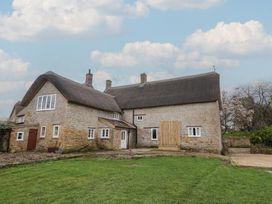 An outdoor view of a stone building with a thatched roof at Manor Cottage in Kingstone near Ilminster